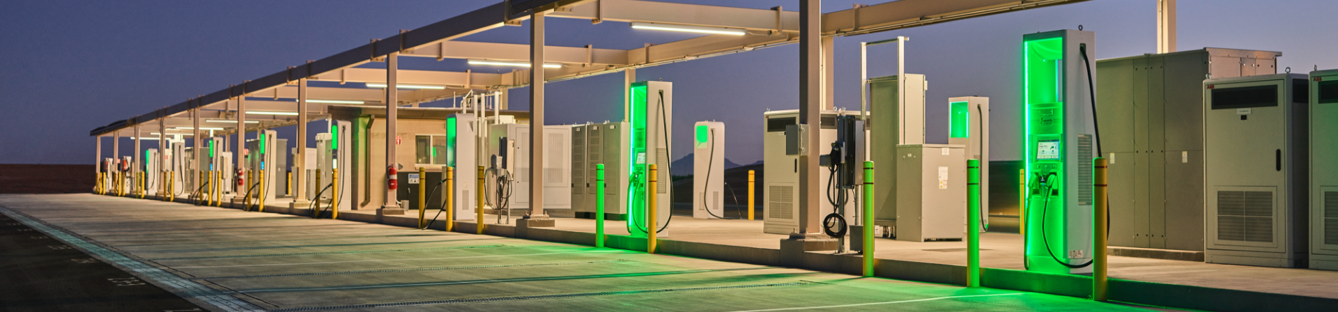 an Electrify America charging location at dusk displaying ten chargers pictured from the corner of the lot